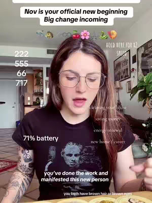 A young woman with long, light brown hair wearing glasses and a graphic t-shirt is centered in the frame, speaking directly to the camera. The background suggests a room with a glimpse of the kitchen. Overlay text includes phrases related to a new beginning and tarot reading, along with several numbers. The woman's arms and the lower part of the frame are also visible, revealing her attire and the location.