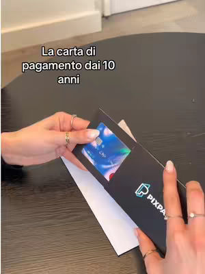 A person's hands are holding a black Pixpay cardholder, revealing a colorful payment card. Text in Italian is overlaid at the top.