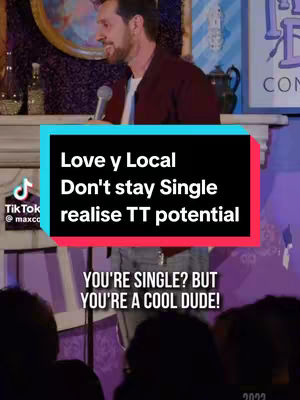 The cover image shows a man on a stage with a microphone, likely a stand-up comedy setting. In the foreground, the bottom of a group of people facing stage. A rectangular, black-and-red text box overlay has text related to dating or relationships appears to be added near the man in the center of the image.. The background is blurry, suggesting a room, and it contains what looks like a painting and some equipment and bottles.