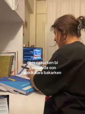 A young woman with her hair pulled back is sitting at a desk in front of a computer. She is writing in a notebook with a pen, and the screen shows various windows. The text overlay reads in Turkish.