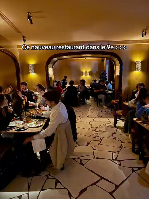 The cover image shows a restaurant interior with multiple people seated at tables. The lighting is warm, and the decor includes ornate wall sconces and a patterned floor. A text overlay in French is present.