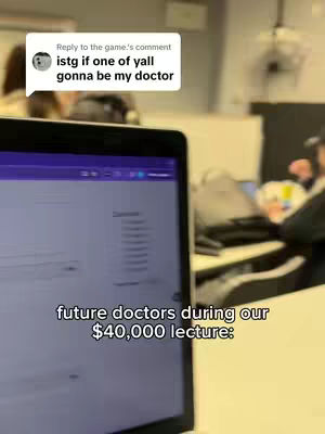 A laptop screen is in focus with text overlayed on it. The bottom portion of the screen is visible displaying text in white, with a blurred background of a classroom setting. Above, a comment box containing text is visible. Several people attend the class, one is visible on the left blurred. The whole image gives a feel of a college lecture.