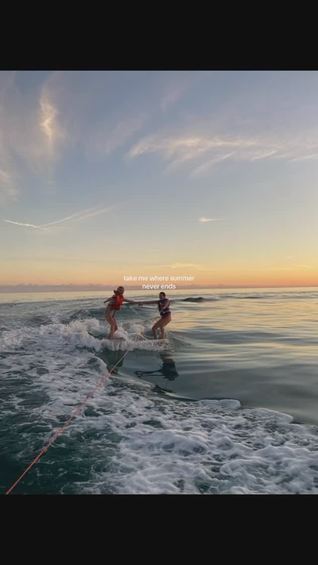 Two women are waterskiing on a lake at sunset. The sky is a gradient of blues and oranges.