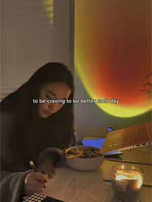 A person writing at a desk with a bowl of food, a lit candle, and a special light fixture creating a sunset effect.