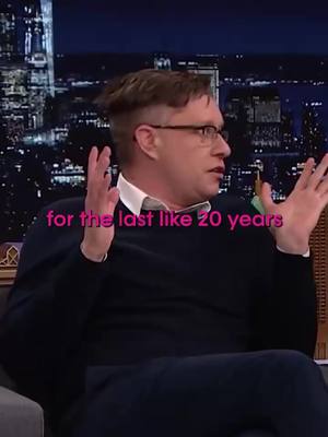 The cover image shows a man on a set, speaking with visible hand gestures. Text overlayed on the image mentions a time frame in relation to a topic, with a city skyline blurred in the background.