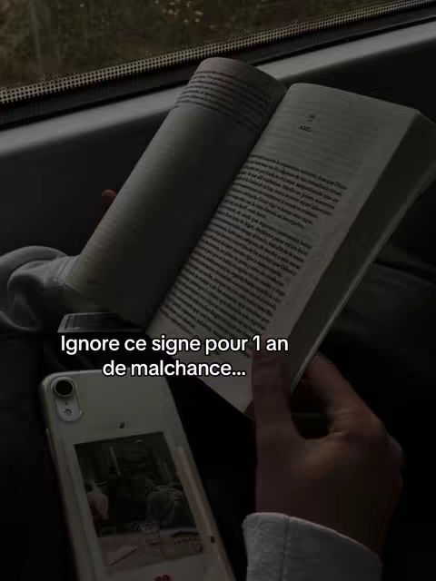 A person is holding a book and a phone, appearing to be on a train. The lighting is dim, creating a somber mood with the dark gray of the train interior.