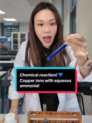 A woman in a white lab coat holds a test tube filled with vibrant blue liquid with an excited expression. There's text in a colored box at the bottom indicating it's a chemical reaction with copper ions and aqueous ammonia.