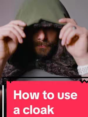 A man with long hair and a beard is the central focus, his face partially obscured by a dark, hooded cloak. He's holding the hood up with both hands. Below him, a red banner displays white text: "How to use a cloak."