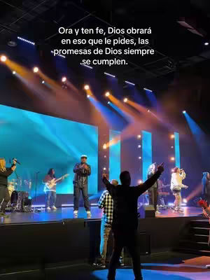 A live performance on a stage with multiple people. The lighting is bright, and there is text overlayed.