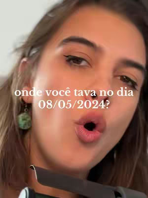 A selfie-style shot featuring a woman with blurred background. She has light skin, dark eyeliner, and visible earrings. Her mouth is open, and she appears to be speaking or reacting, with a focus on her expression.