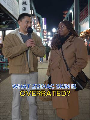 A night scene on a city street with two people. A man on the left is holding a microphone and the woman on the right is looking at him. Text overlayed. The setting is commercial with lights and shops on either side.