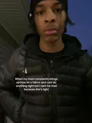 A young Black man is centered in a vertical video frame, looking at the camera with a subtle expression. He wears a black beanie and a black jacket, which suggests a cold outdoor setting. Text over the image states a relatable sentiment about a mother's comments on perceived failures.