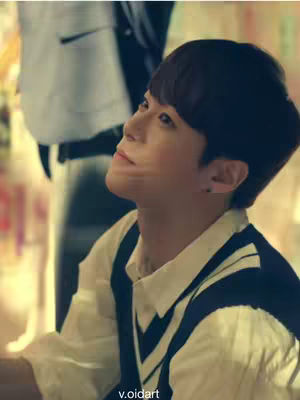 A medium shot of a young man looking up with a wistful expression. He's wearing a white collared shirt with a dark blue vest, set against a blurry background. The lighting is soft, and the man's gaze is directed upwards, giving a sense of longing or thought. The bottom of the image also features a watermark.