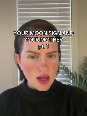 A woman is in the foreground, framed from the chest up, against a softly lit indoor background. She has fair skin, light-colored eyes, and is wearing a dark sweater. The overlay text declares 'Your Moon Sign and Your Mother pt. 1'.