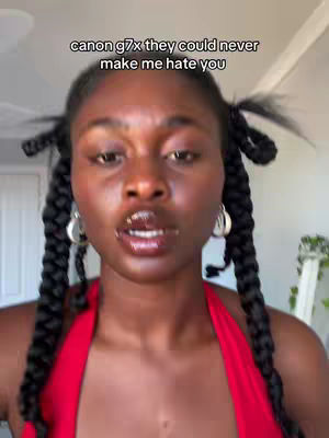 The cover image features a close-up shot of a woman's face. She has dark skin, dark braids, and is wearing silver hoop earrings. The woman's lips are glossy, and she appears to be speaking. The top of a red top is visible. Text appears at the top: "canon g7x they could never make me hate you."