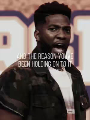 A medium shot of a Black man with short, dark hair, wearing a black jacket over a white t-shirt. The man is shown from the chest up, with a concerned and expressive face, mouth open as if speaking passionately. Overlay text is present on the image.