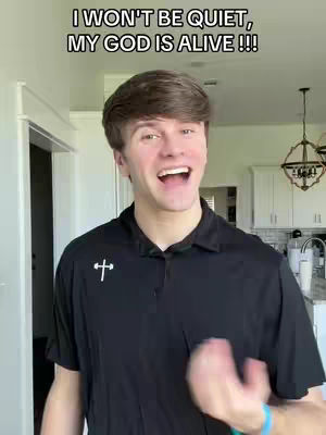 A young man with brown hair and a black polo shirt with a cross logo is smiling widely with his mouth open, seemingly mid-sentence or laughter. The background is a bright interior space, potentially a home, with a white door frame and glimpses of a kitchen area, including a light fixture. The lighting appears natural and bright, highlighting the man's face and expression. Text overlays the image.