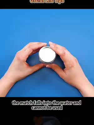 The cover image shows a vertically oriented video still. In the top section, there is a text overlay that reads 'Useful Life Tips' in a clean, white font, set against a dark background. The middle section features a close-up shot: a small, silver-lidded container is held by two hands against a solid blue background. The hands are fair-skinned, and the container appears to be at the focal point. Below, a black text overlay informs viewers about the video's content with the words: 'the match falls into the water and cannot be used'. The bottom portion fades into black.