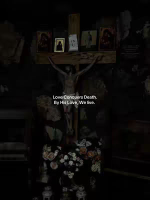 The image shows a dark interior with a depiction of Jesus on the cross as the central focus. A wooden cross holds the figure, with arms outstretched. Above the figure are framed traditional religious images. Below the cross are flowers. Text is superimposed on the image.