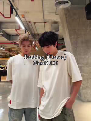 Two young men stand in a well-lit room, likely a dance studio or rehearsal space. The man on the left has light-colored hair while the man on the right has dark hair. Both are wearing similarly colored loose-fitting t-shirts and casual pants. Text overlayed on the image says "Ranking (Dance) Next1DE."