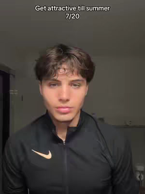 A young man is centered, looking directly at the camera with a neutral expression. He has short, dark brown hair and light skin. He wears a black zip-up jacket with a Nike logo on the left chest. The background is a plain, dark gray. Above his head is text in a simple font.