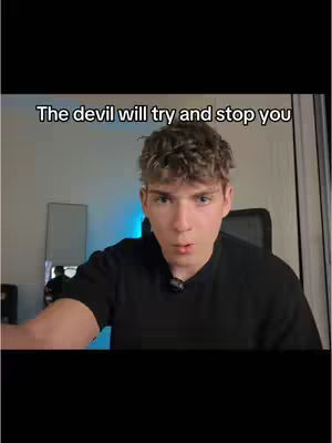 The image shows a young man facing the camera, with text overlaid at the top. He has short, light-colored hair and is wearing a black shirt. The background includes a glimpse of a room with a light fixture and some electronic equipment, with a blue-toned light source adding depth. The composition is simple, focusing primarily on the subject and his expression.
