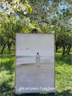 A person holds up a framed painting, obscuring their body. The artwork depicts a figure walking toward the sea, with birds in the sky. The background shows a vibrant outdoor setting with blooming trees. The overall tone is serene and reflective.