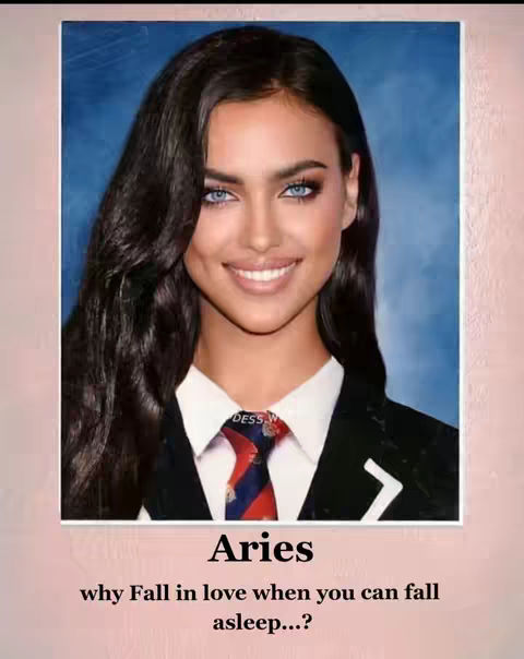 A studio-style image of a woman with long dark hair and striking blue eyes, smiling slightly. She's wearing a suit jacket over a white collared shirt and a patterned tie. The background is a faded blue.