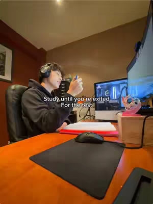 A young man is sitting at a desk with a computer screen, headphones, and study materials, giving a motivational vibe.