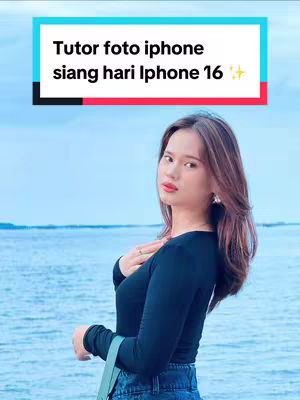 The cover image showcases a young woman posing outdoors with a backdrop of the sea under a cloudy sky. She's wearing a black long-sleeved top and jeans, with a light green bag slung over her shoulder. A text overlay in a blue and white rectangular box at the top reads, "Tutor foto iphone siang hari iPhone 16", indicating a tutorial related to iPhone photography, possibly with the iPhone 16.