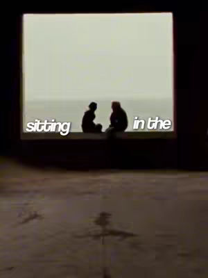 The cover image shows a view through a rectangular opening. Two silhouetted figures are seated on a ledge, with a background of a light-colored sky and water. Text overlays the image.