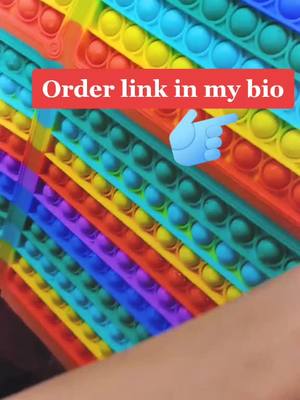 The image displays a close-up of a colorful pop-it toy, with rectangular sections divided into diagonal stripes of various colors, each section filled with circular bubbles. A red banner with white text overlays the toy, and a hand icon pointing towards the text is also included.