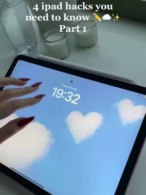 The cover photo shows an iPad with a blue sky wallpaper featuring heart-shaped clouds. The hand of a person with red nail polish is visible, interacting with the tablet. The top displays the time, and various objects like a glass and a jar are slightly out of focus in the background.