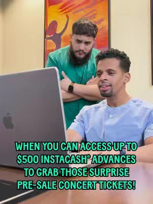 Two men are shown in a room with a laptop. The man in the foreground is sitting and looking at the laptop screen. In the background, another man is standing with arms crossed, looking over the first man's shoulder. There is a colorful painting on the wall behind them. Text is overlaid at the bottom of the image.
