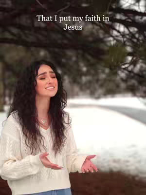 The cover image showcases a woman with long, dark wavy hair singing with her eyes closed and hands outstretched. She is wearing a white sweater and a delicate necklace. The background presents a blurred view of trees and snow, suggesting an outdoor winter setting. Text at the top reads, 'That I put my faith in Jesus'.