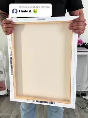 A person holding a white canvas. The canvas is rectangular and has a wooden frame. The person is wearing a black shirt and blue jeans.