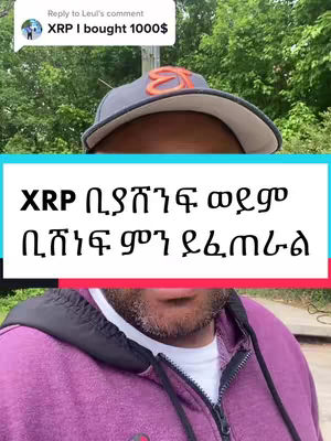 A selfie-style video cover with the upper portion of a person visible. The person is wearing a grey cap with an orange logo and a purple hooded sweatshirt. A text overlay in a white box with a black border reads 'XRP ቢያሸንፍ ወደም ቢሸነፍ ምን ይፈጠራል'. Above the overlay is a comment bubble containing text beginning 'XRP I bought 1000$' and a profile picture.