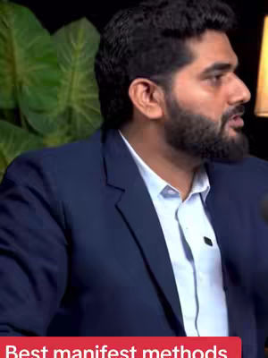 A man with a beard is featured, dressed in a blue suit over a light blue shirt. The background is out of focus, and there's text at the bottom. The lighting suggests an indoor setting.