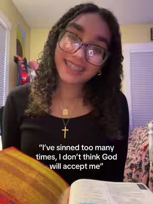 A young woman with curly hair and glasses is smiling directly at the camera, appearing to be in a room with a soft yellow wall and a window. She wears a cross necklace and a black top. The text overlay in the bottom of the image reads a quotation.