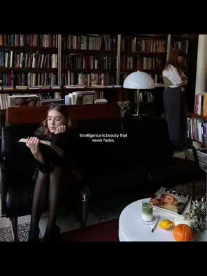 A woman sits on a black sofa in a library, reading a book. The background is filled with bookshelves. A white table holds a drink and magazines, with a quote overlaid on the image.
