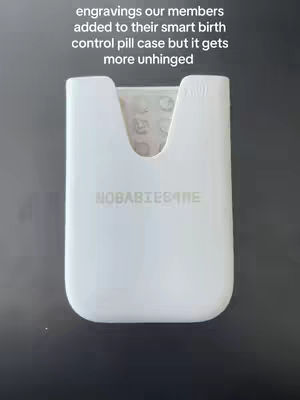 The image features a white pill case with rounded edges and a cutout at the top. The text overlay reads: 'engravings our members added to their smart birth control pill case but it gets more unhinged'. Below the cutout, it says 'NOBABIES4ME'. The background is a dark gray.