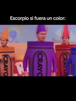 The image shows a scene from a TV show or a skit. Several people are dressed in crayon costumes of different colors. The main subject is dressed in a purple crayon costume with the word 'CRAYOLA' on it, centered and slightly above the other crayon people in orange, red and blue. The background has colors.