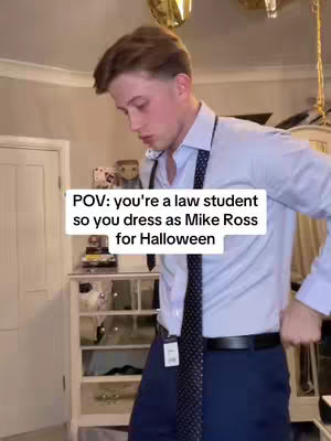 A young man posing in a room, dressed as the character Mike Ross from "Suits," with a white text overlay. He wears a light blue dress shirt with a dark tie.