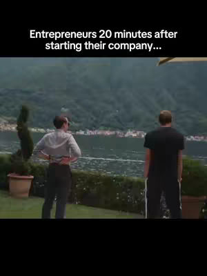 Two men stand outdoors, looking towards a body of water, framed by greenery and a mountain range in the background. The image has text overlay at the top.
