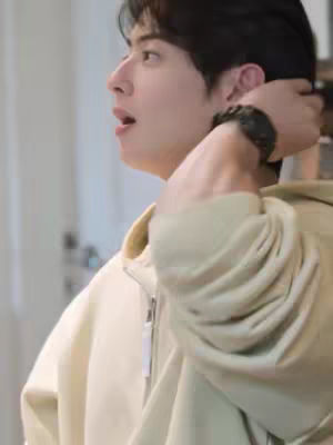 The cover image shows a side profile of a young Asian man, likely in his twenties. He is looking towards the left with his mouth slightly open, as if he's speaking or surprised. His dark hair is neatly styled, partially covering his forehead. He is wearing a light-colored zip-up hoodie. His left arm is raised, with his hand near the back of his head. The background is blurred, suggesting an interior setting with neutral colors.
