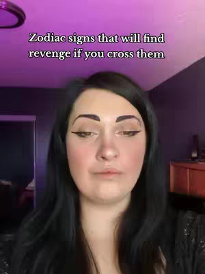 A woman is centered in a medium shot, framed from the chest up. She has long black hair, dark eyebrows, and is wearing makeup including eyeliner. The background is a blurry, purple-toned interior. The text overlay reads:
"Zodiac signs that will find revenge if you cross them."