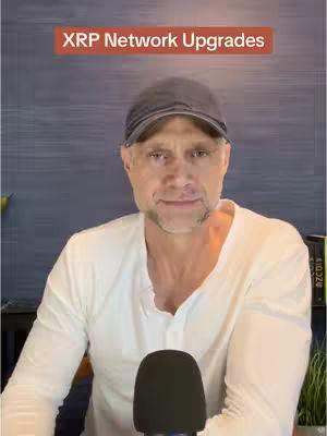 A man in a white shirt and a dark baseball cap is seated in front of a microphone. The background is a textured blue wall, and the text 'XRP Network Upgrades' is displayed in a red box above the man's head.