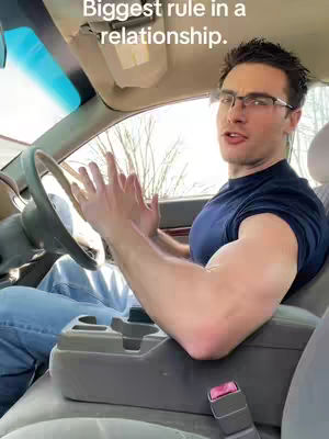 A man is sitting in the driver's seat of a car, looking towards the camera with an open mouth and hands clasped together. The text overlay reads, "Biggest rule in a relationship."
