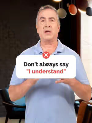 A medium shot focuses on a man, positioned from the chest up, set against a blurred background that features a dark wall and some decorative lighting. The man is looking directly at the camera and speaking. Overlayed on the image is a white rectangular speech bubble with rounded corners that feature the text overlayed. A red 'X' is above the text.