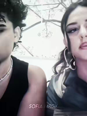 The cover image shows two young women, their faces close-up. The woman on the left has dark, curly hair and is wearing a black top and a silver necklace. The woman on the right has her hair pulled back, large hoop earrings, and dark eye makeup. They appear to be outside with blurry tree branches in the background. The color palette is muted, with a focus on skin tones and dark clothing.